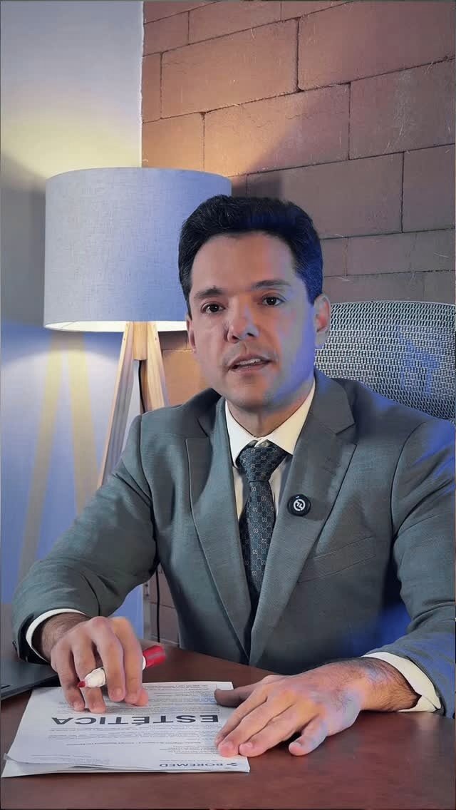 Caico Borelli à mesa do escritório, com uma caneta sobre uma carta, luminária acesa e parede de tijolo ao fundo