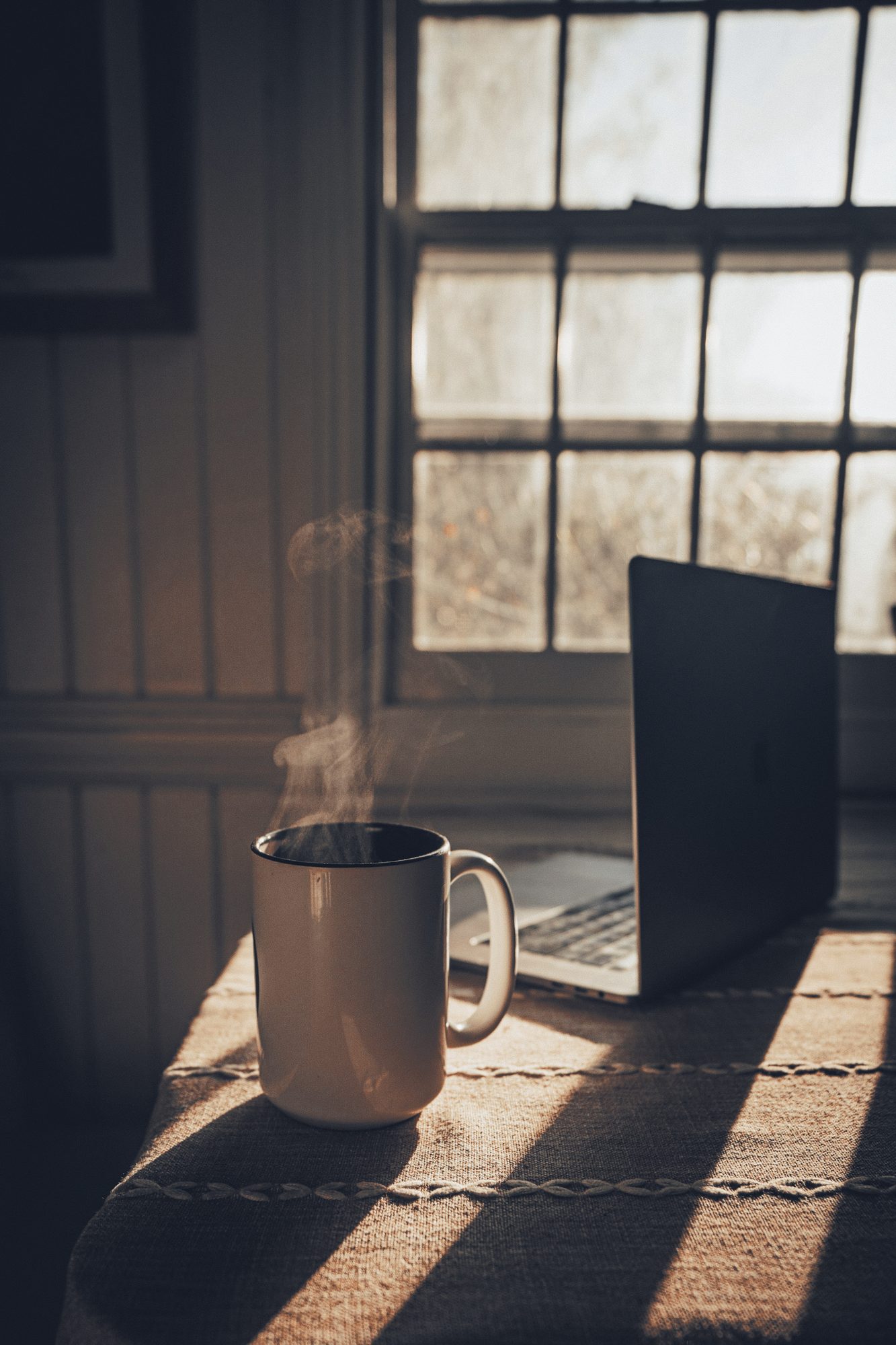 Caneca de café ao lado do notebook, luz de janela desenhando a mesa