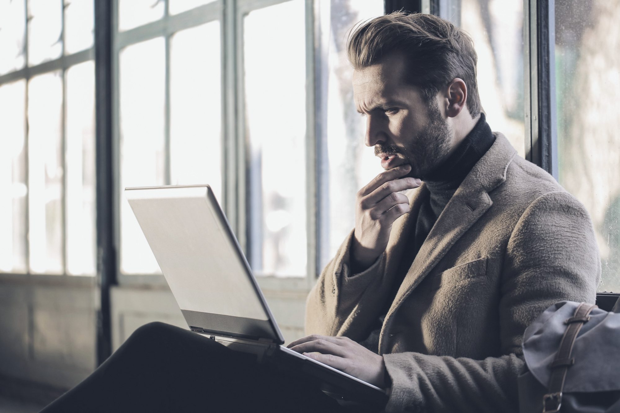 Dono de empresa com a mão no queixo diante do notebook, luz de janela
