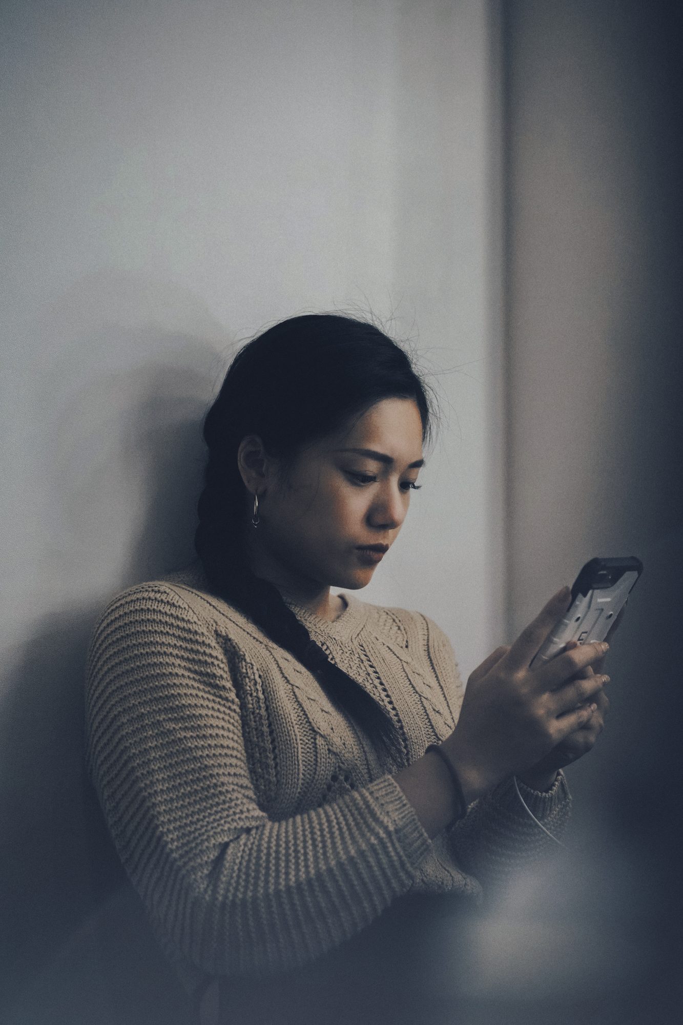 Mulher encostada na parede lendo o celular, luz baixa