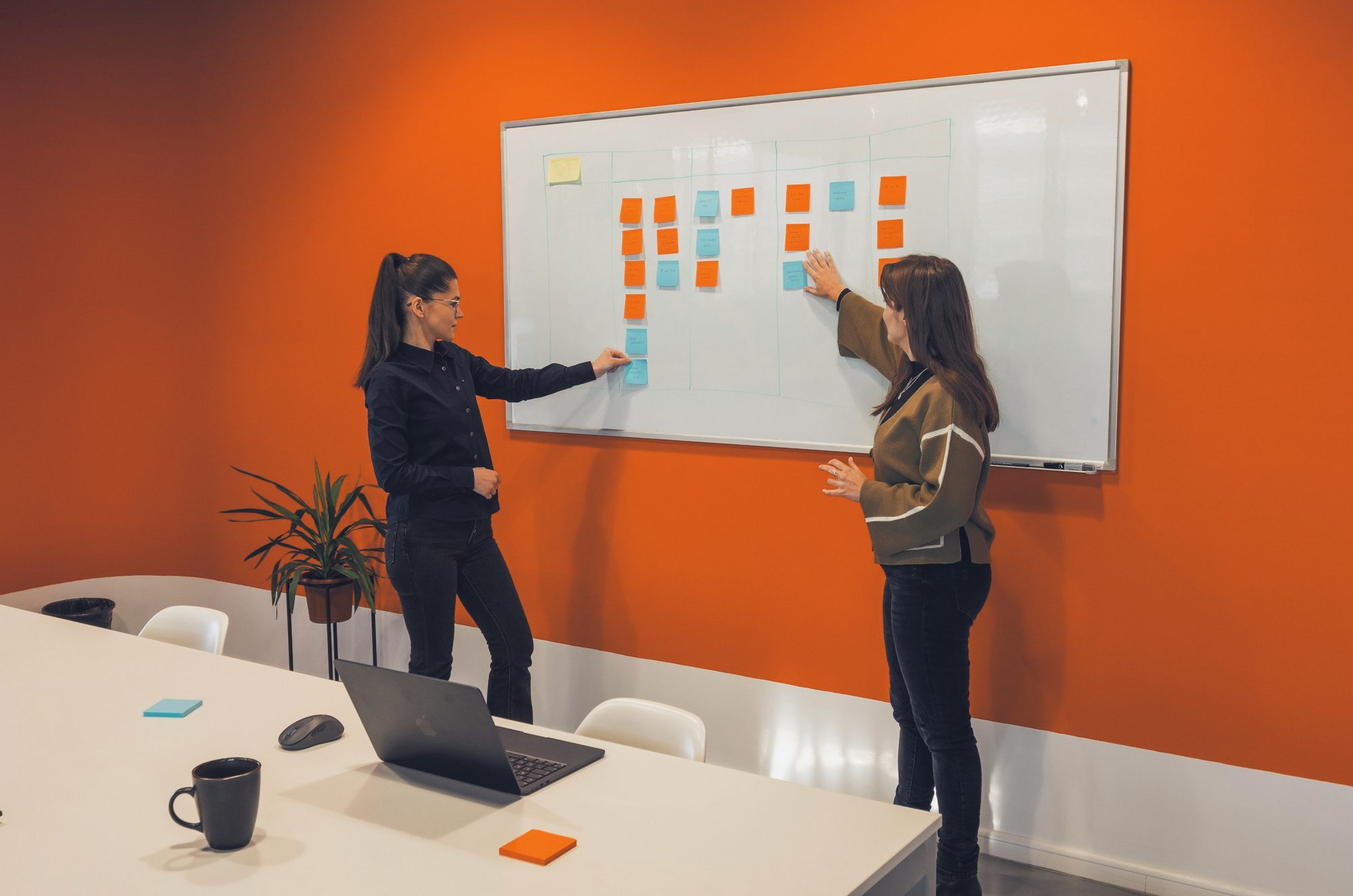 Duas mulheres organizando o quadro de tarefas numa parede laranja
