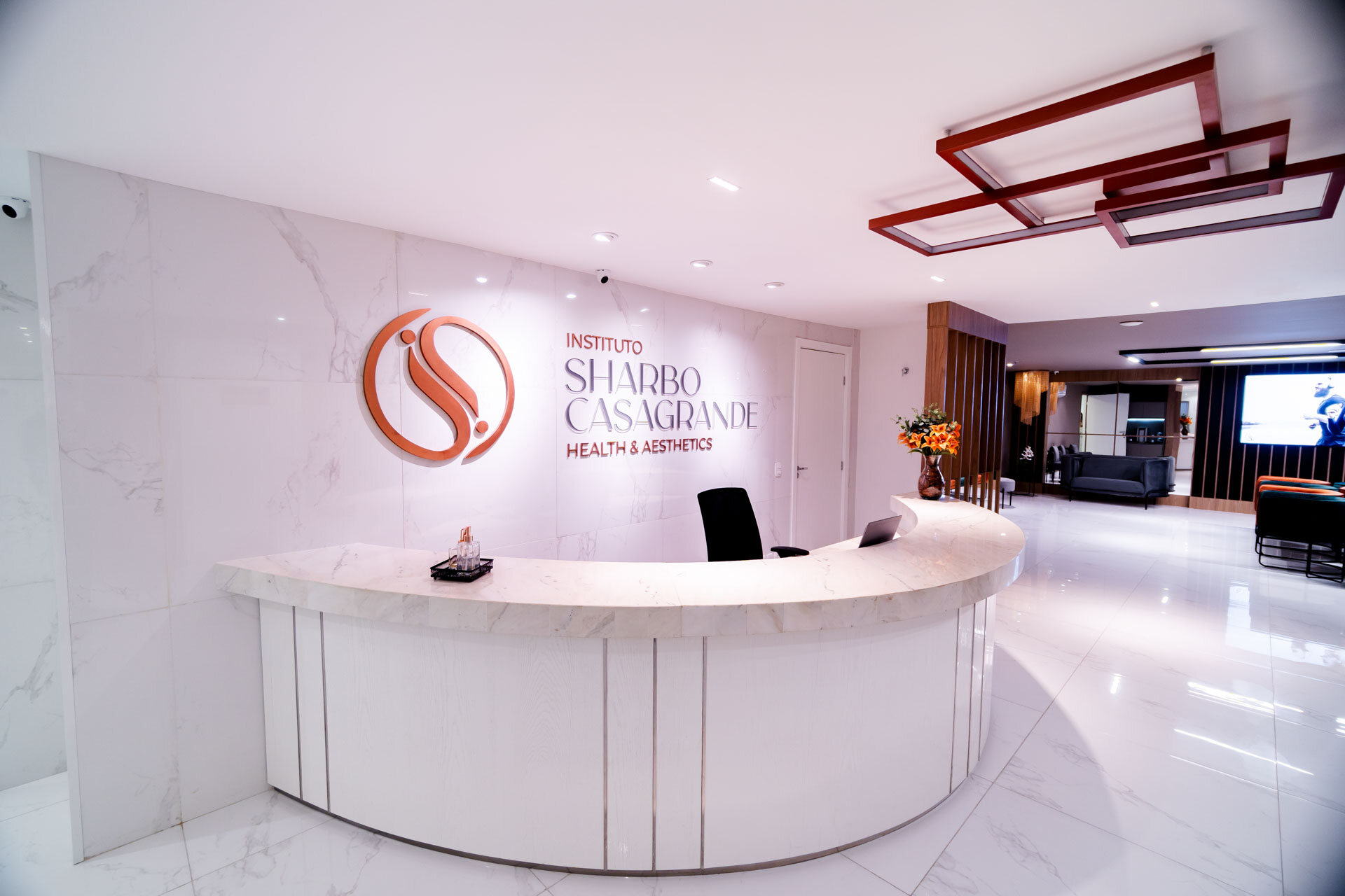 Recepção do Instituto com balcão curvo de mármore branco e, na parede, o letreiro cobre com o símbolo e o nome antigo, Instituto Sharbo Casagrande, Health & Aesthetics