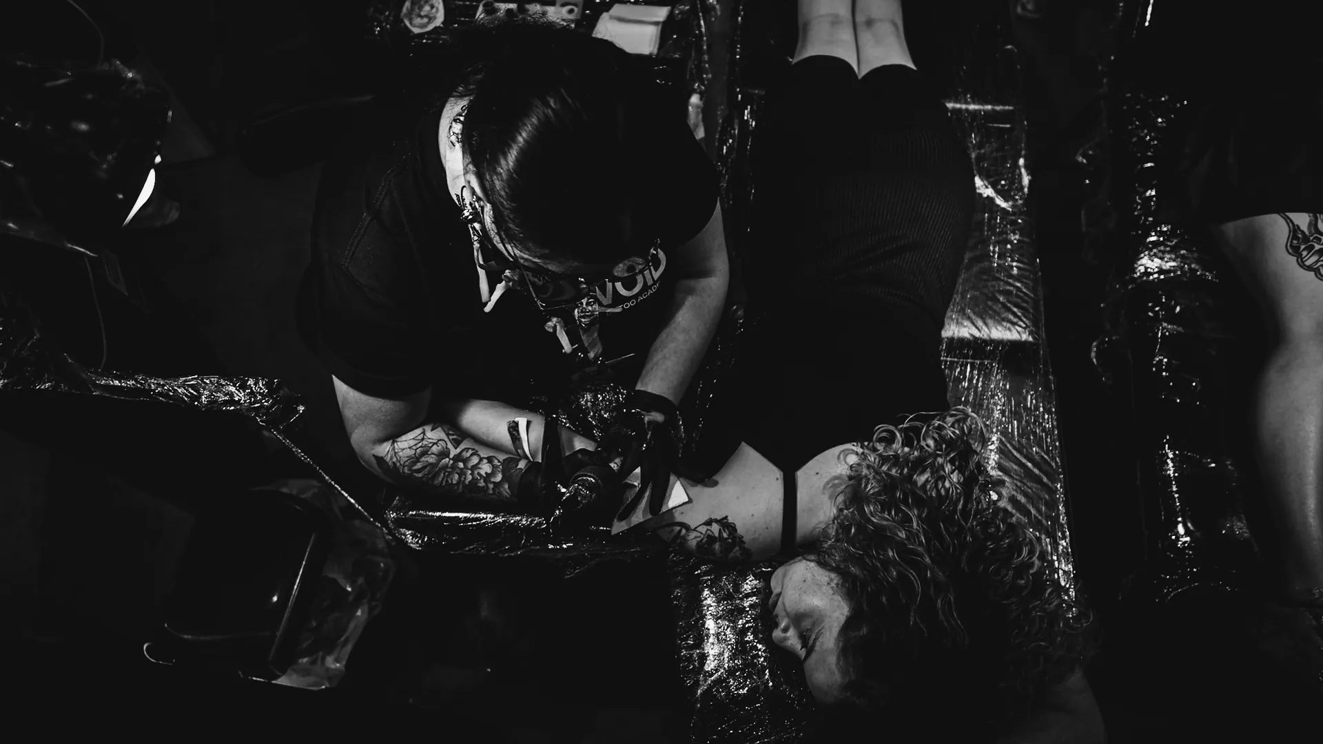 Tatuadora de camiseta The VOID concentrada no trabalho, vista de cima