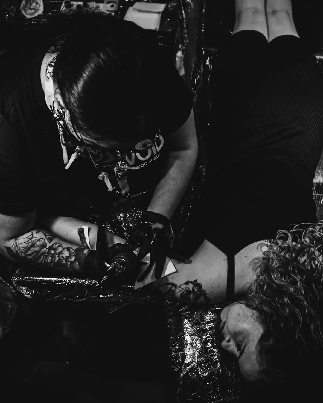 Tatuadora de camiseta The VOID concentrada no trabalho, vista de cima