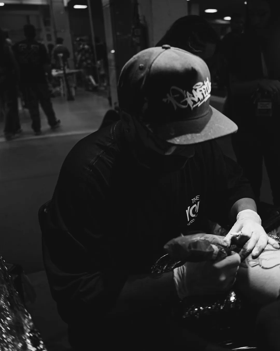 Tatuador de boné tatuando sob luminária durante a convenção
