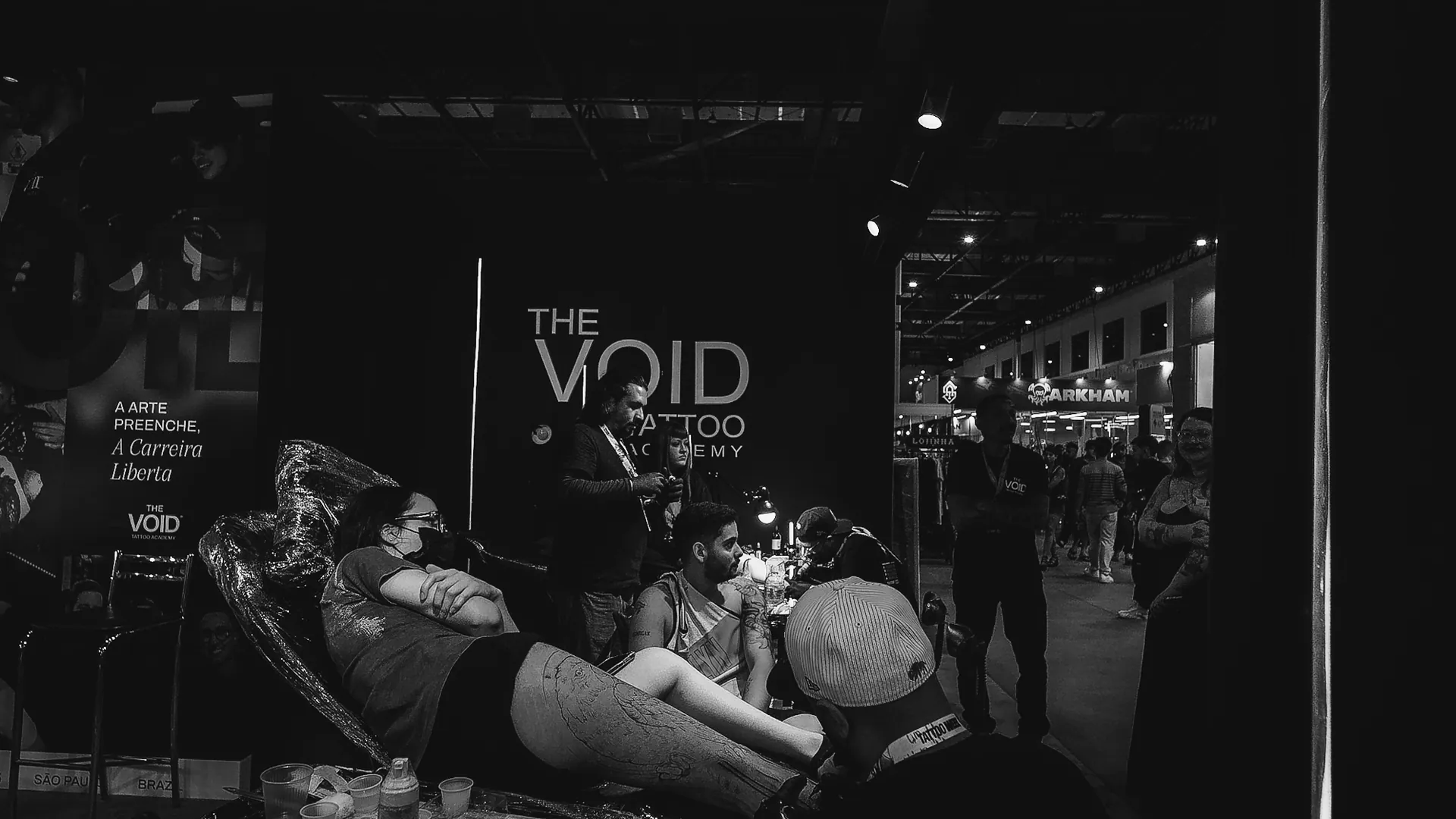 Estande da The VOID na convenção com sessão de tatuagem em andamento e letreiro iluminado