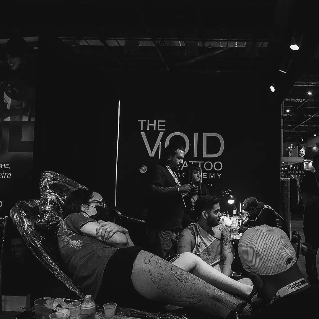 Estande da The VOID na convenção com sessão de tatuagem em andamento e letreiro iluminado