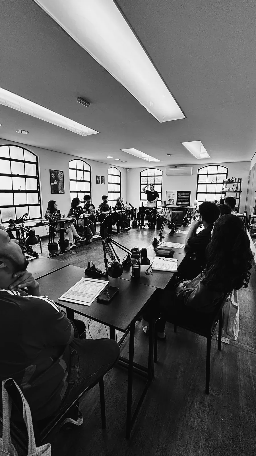 Sala de aula da The VOID cheia de alunos em mesas longas, professor ao fundo