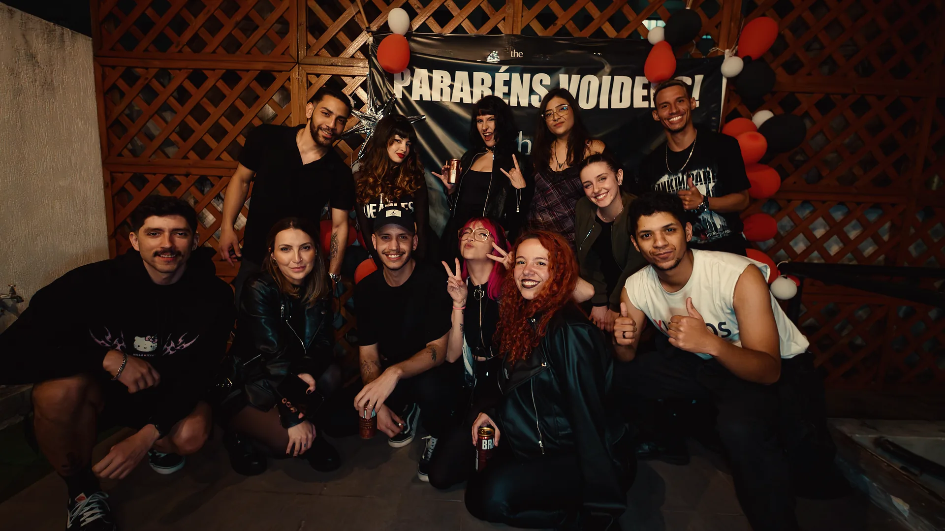 Turma de formatura reunida sob a faixa Parabéns Voiders no terraço da escola à noite