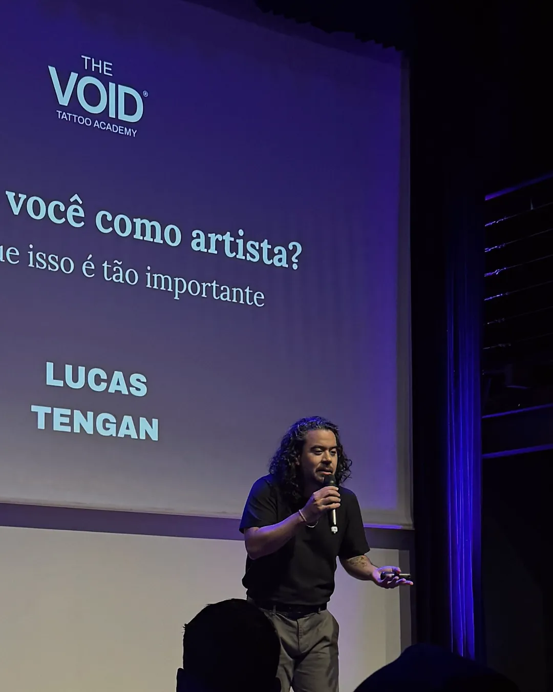 Lucas Tengan palestrando no palco, com o telão perguntando quem é você como artista