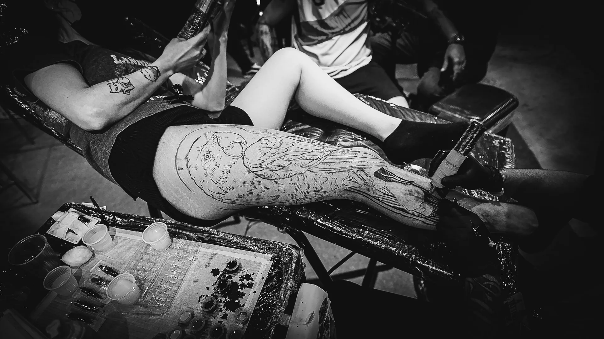 Vista de cima de sessão de tatuagem com perna, máquina e bancada de tintas no estande da The VOID