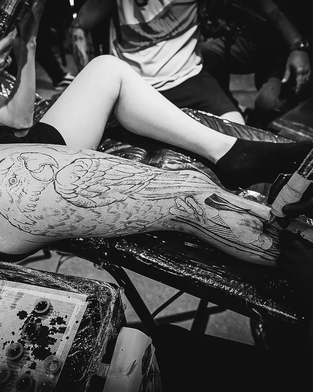 Vista de cima de sessão de tatuagem com perna, máquina e bancada de tintas no estande da The VOID