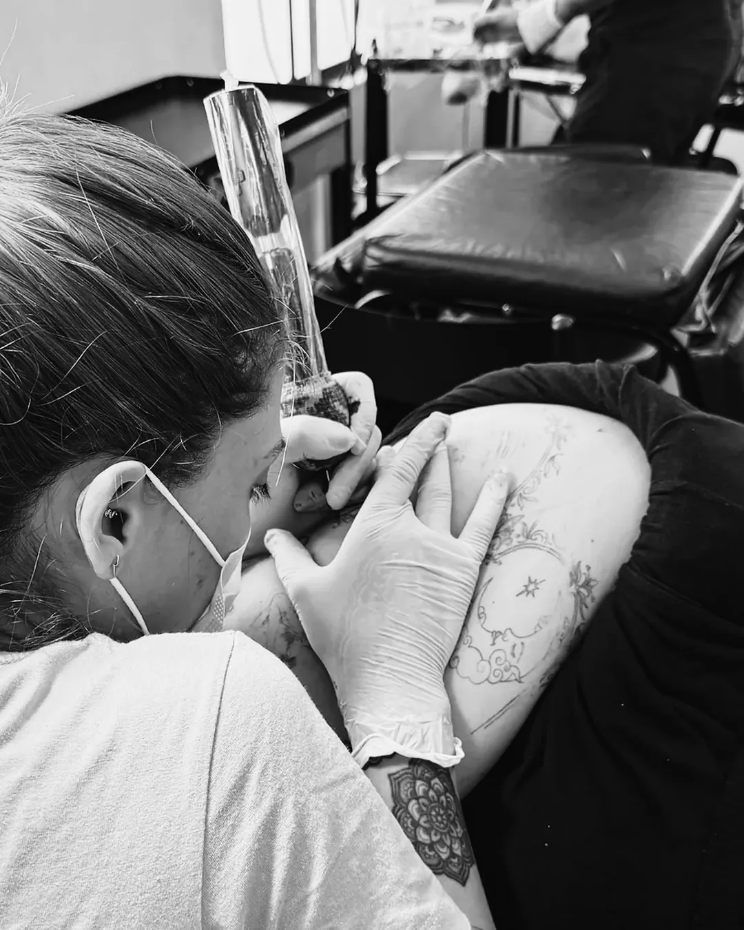 Tatuadora de máscara e luvas nitrílicas tatuando o braço de um cliente na escola The VOID