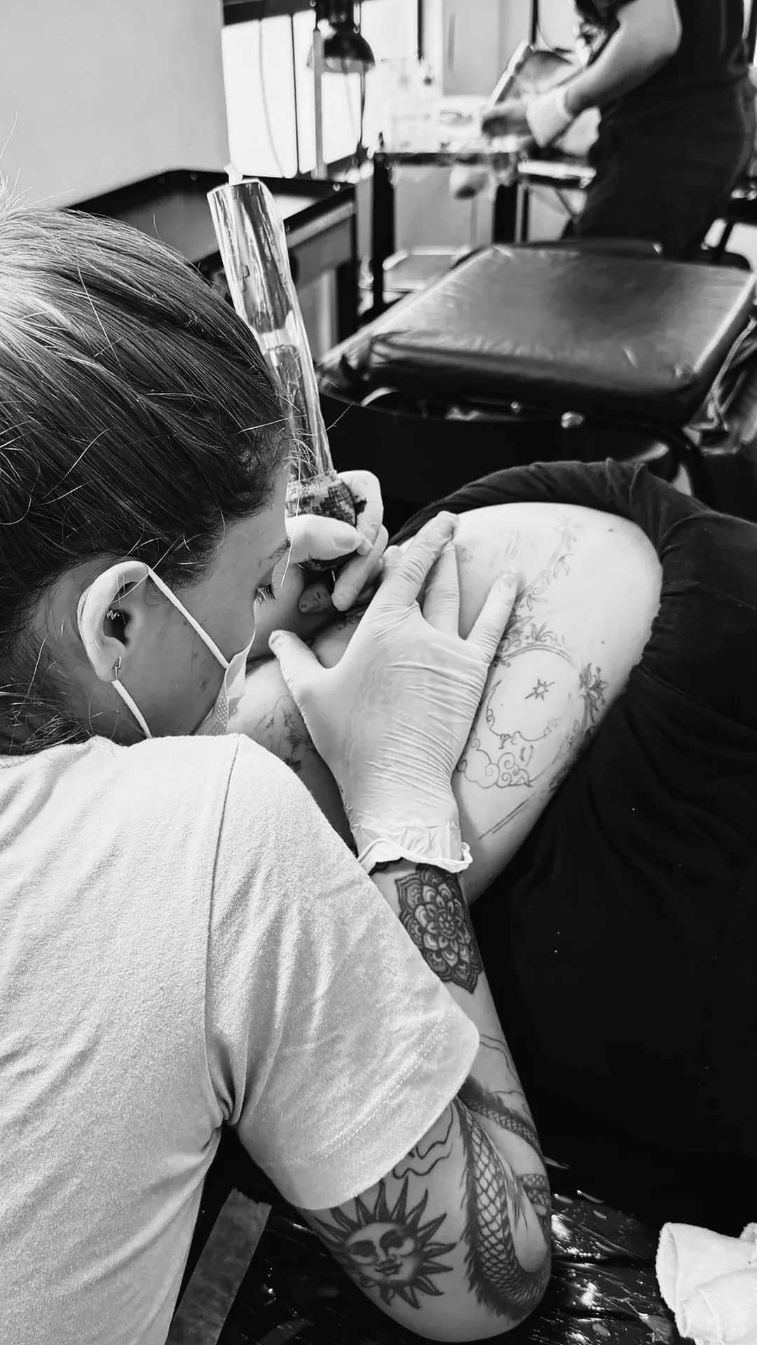 Tatuadora de máscara e luvas nitrílicas tatuando o braço de um cliente na escola The VOID