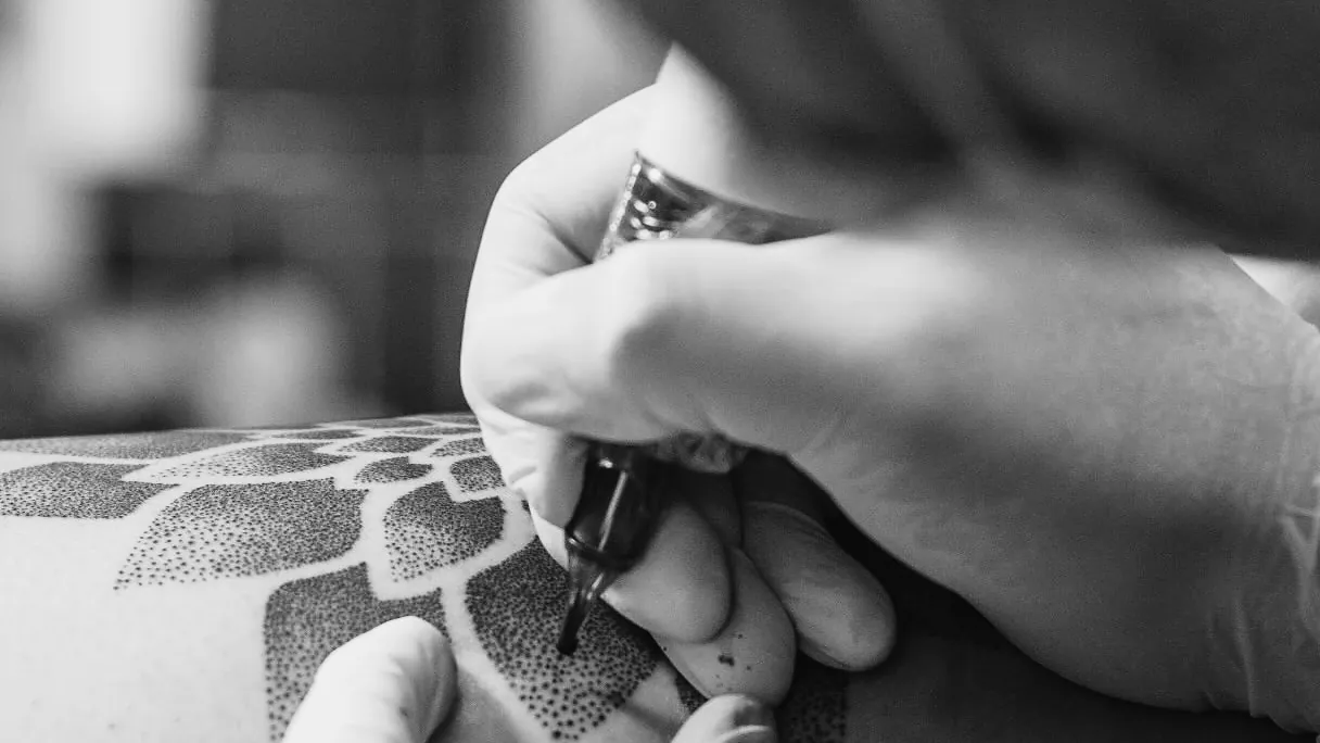 Close de mãos com luvas segurando a máquina de tatuagem sobre a pele durante a sessão