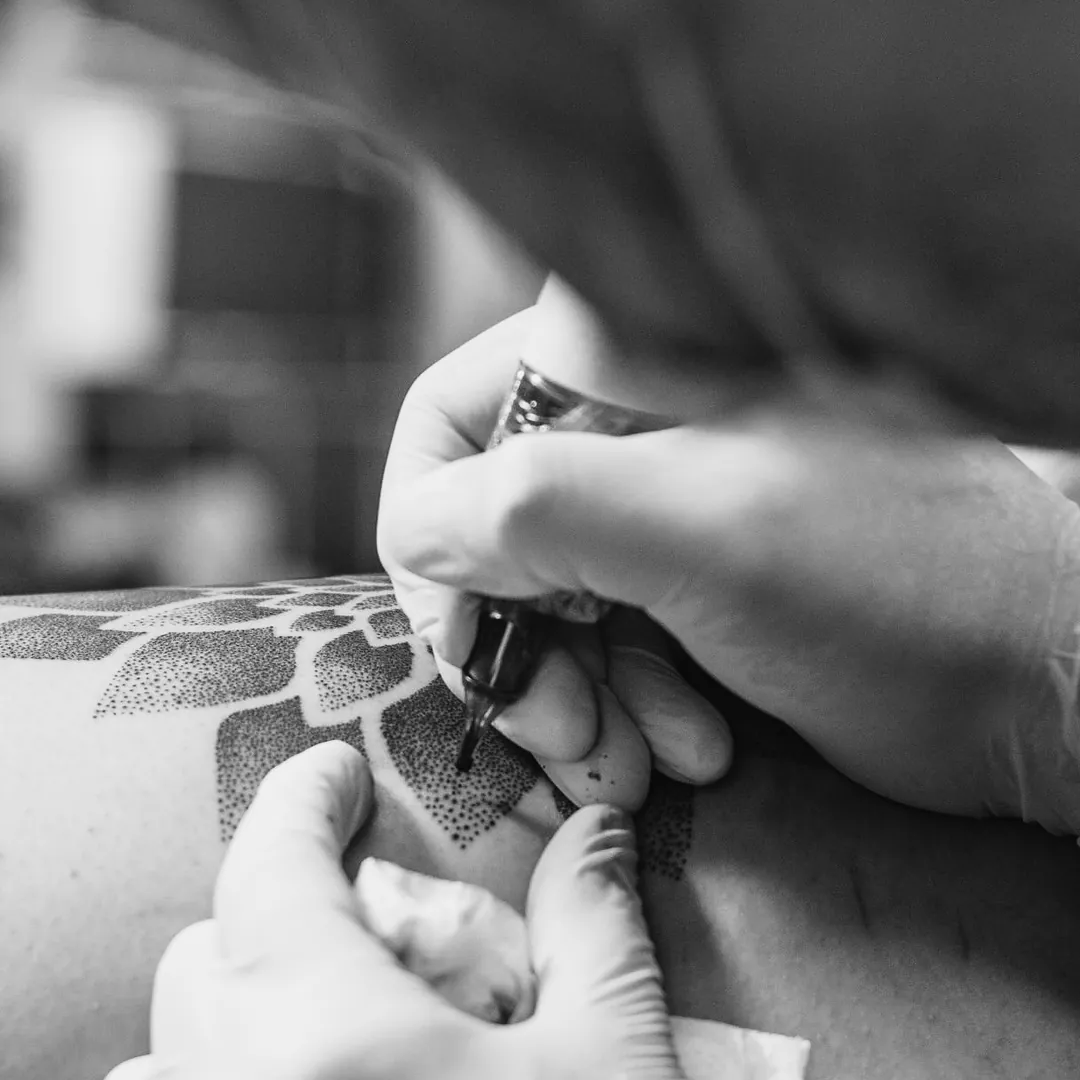 Close de mãos com luvas segurando a máquina de tatuagem sobre a pele durante a sessão