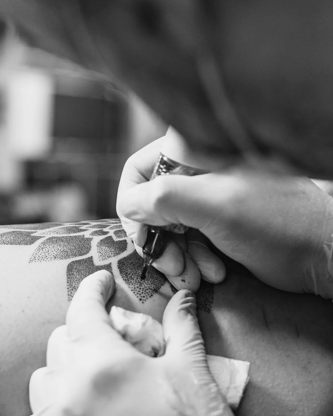 Close de mãos com luvas segurando a máquina de tatuagem sobre a pele durante a sessão