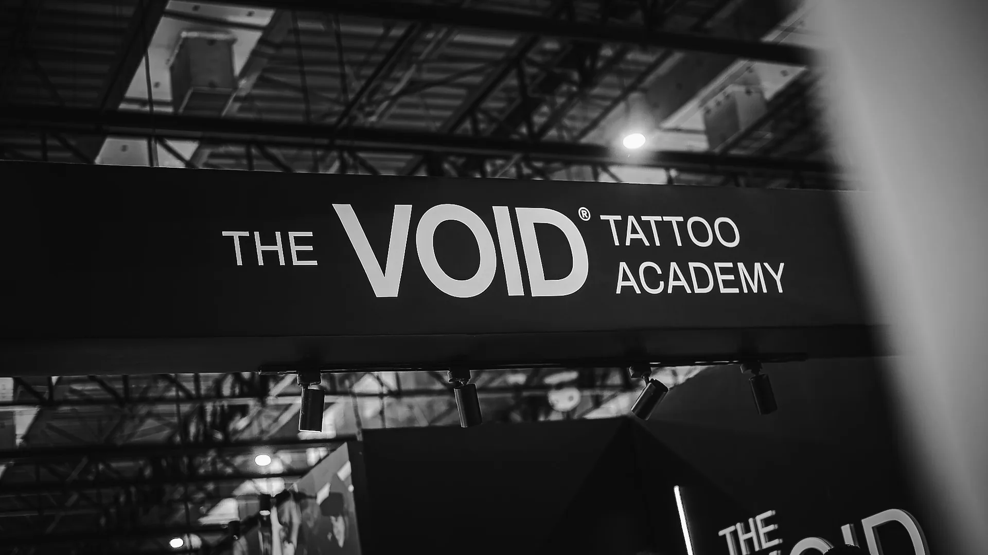 Letreiro iluminado THE VOID TATTOO ACADEMY no estande da convenção, visto de baixo