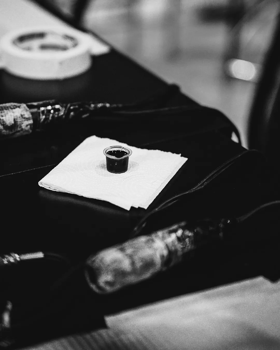Bancada de tatuagem com máquinas pen, batoque de tinta preta e papel toalha sob luz quente