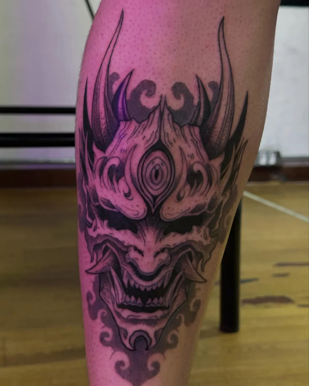 Máscara oni japonesa tatuada na panturrilha, fotografada sob luz rosa