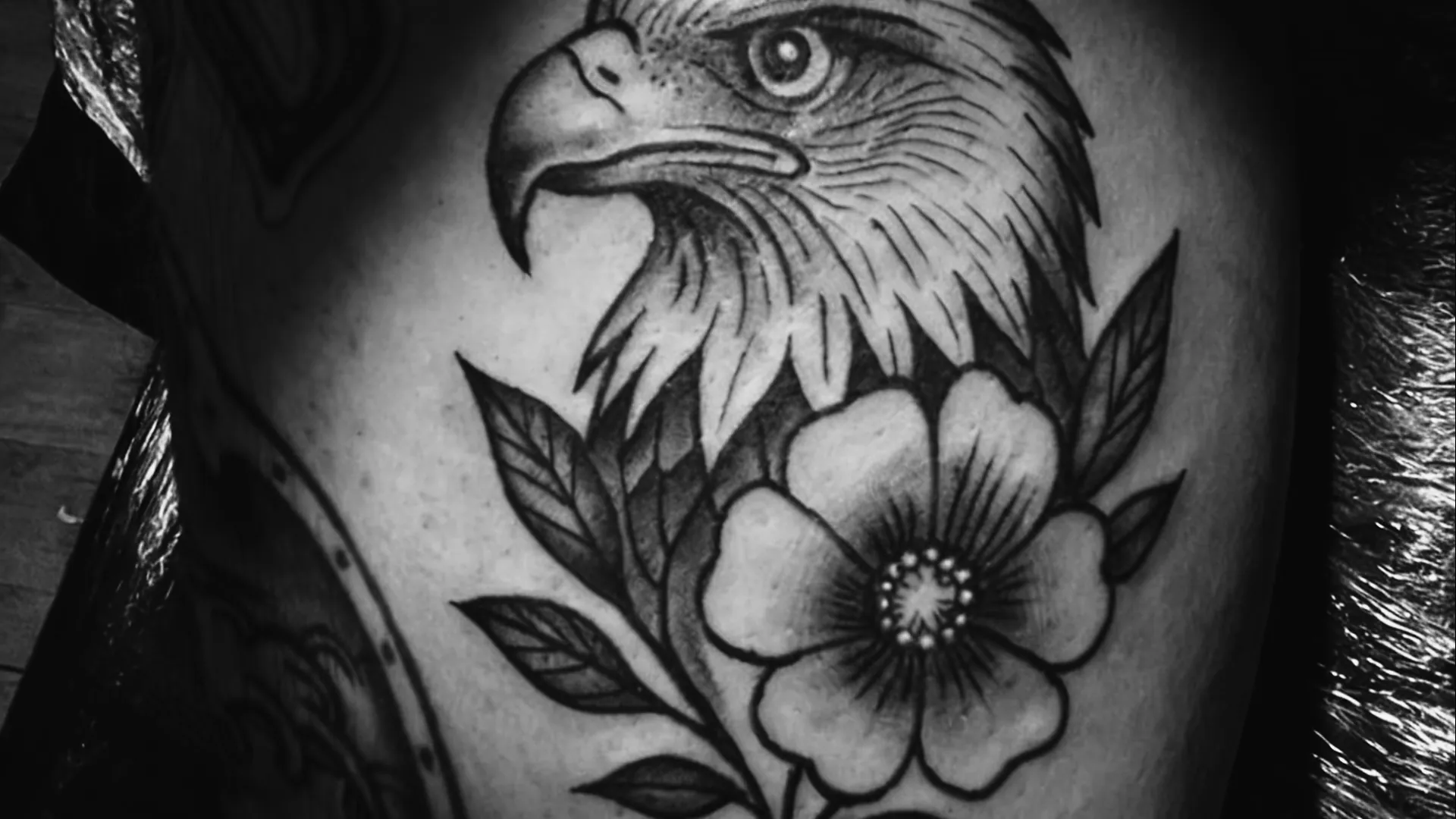 Águia com flor em estilo tradicional tatuada em preto e cinza