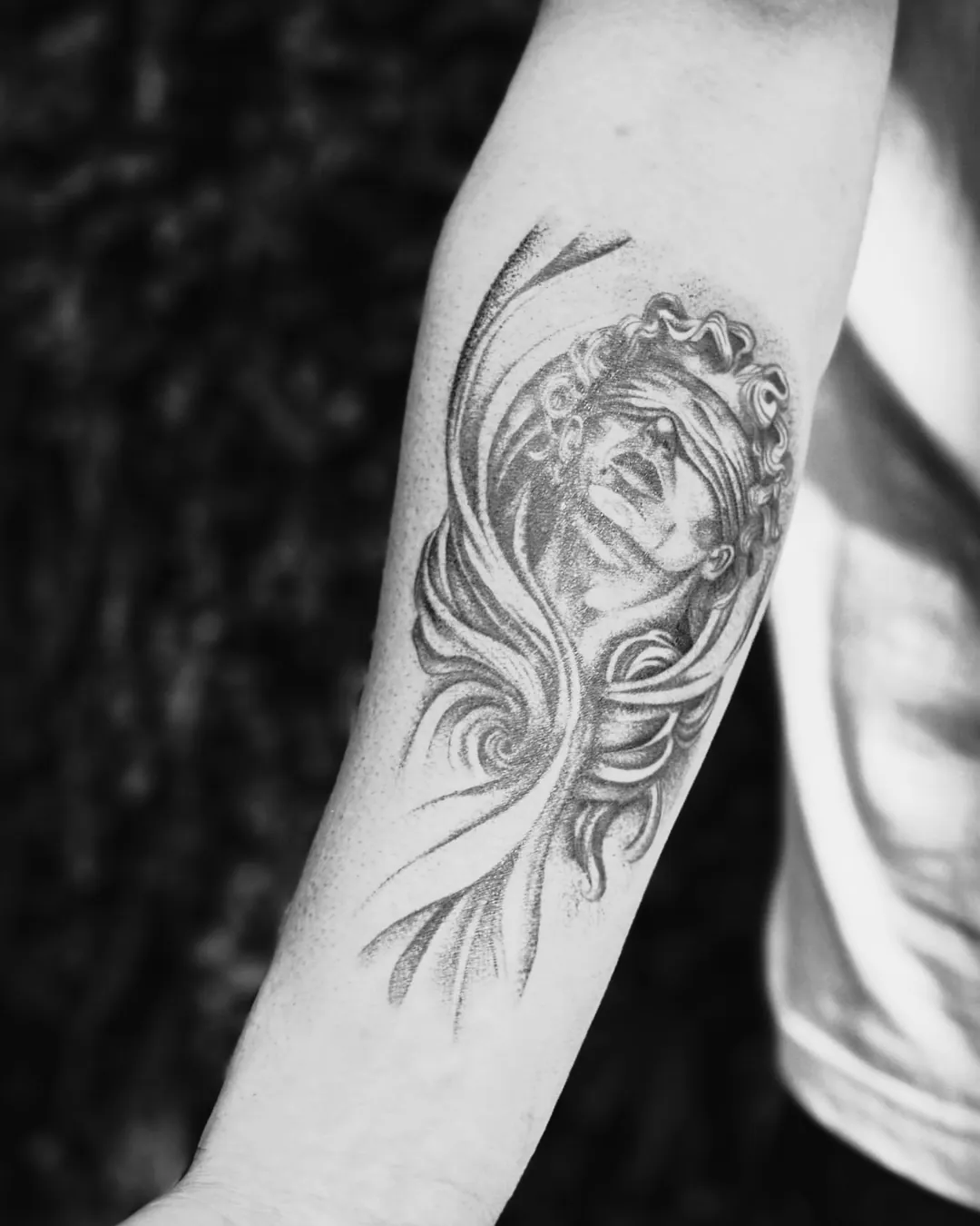 Rosto feminino tatuado em preto e cinza no antebraço