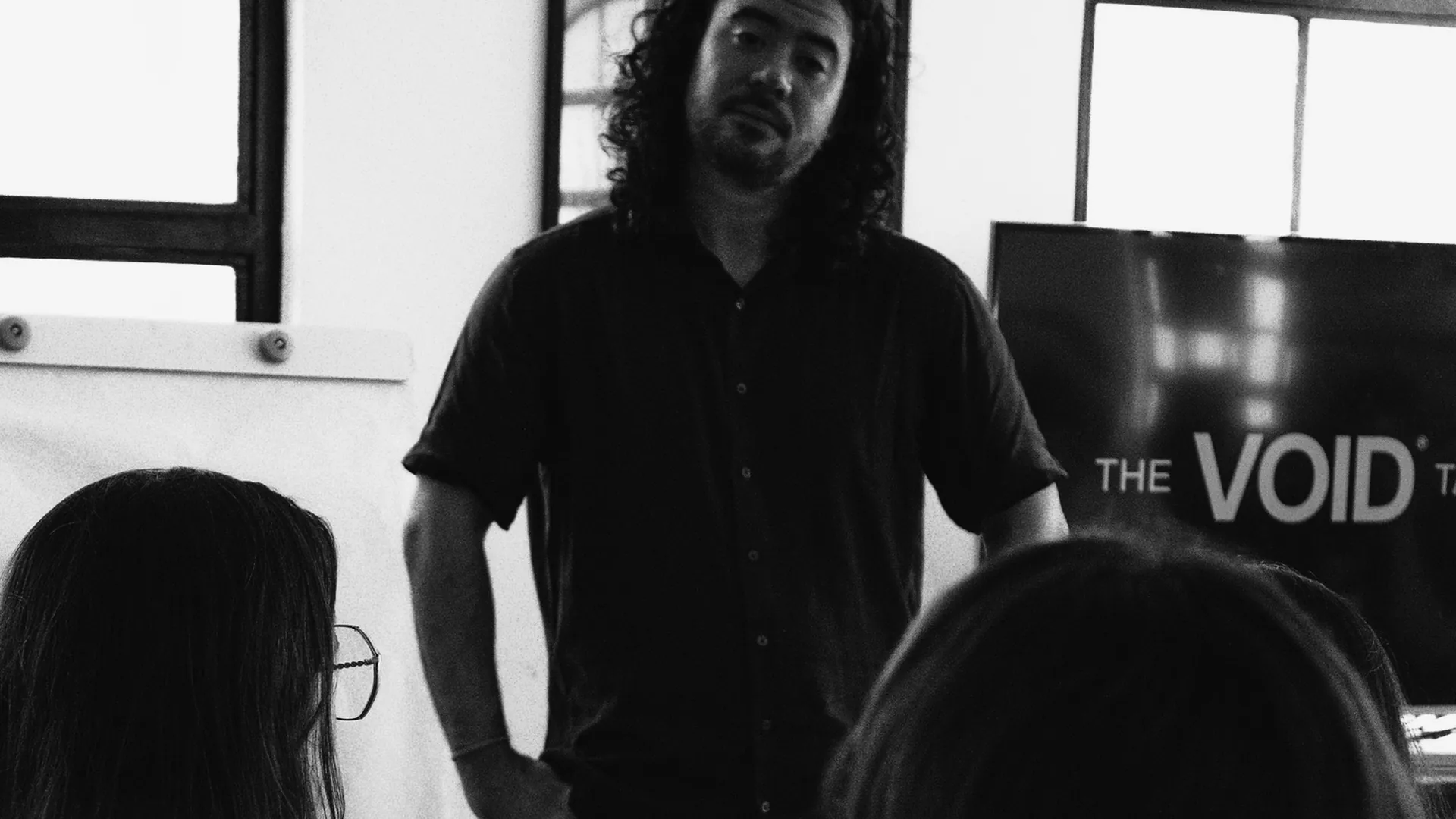 Professor Lucas Tengan em pé falando para alunas sentadas na sala da escola The VOID