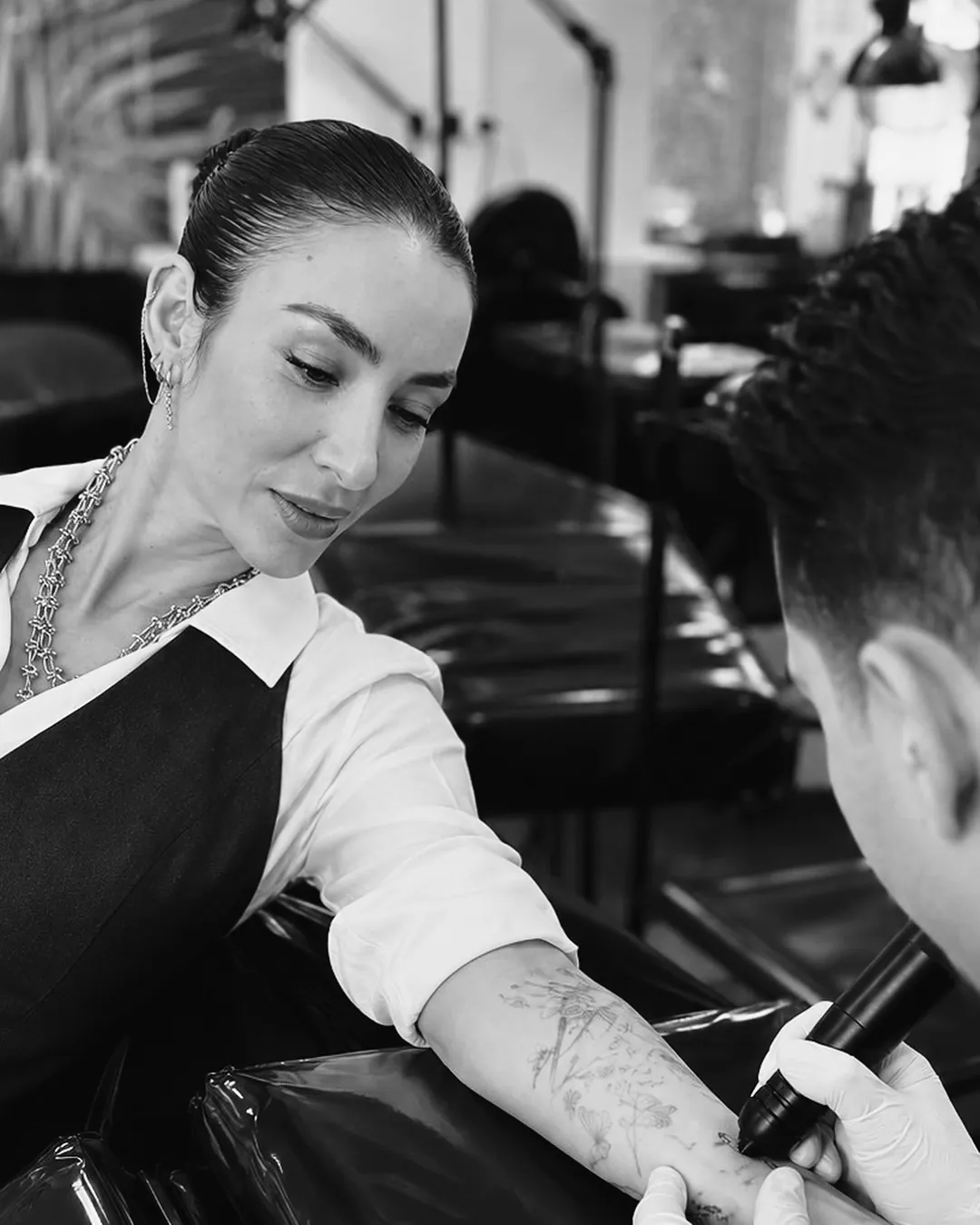 Professora orientando de perto um aluno que tatua o antebraço de outra pessoa