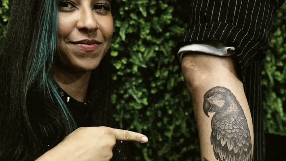 Aluna Açucena apontando para a arara que tatuou na panturrilha da cliente