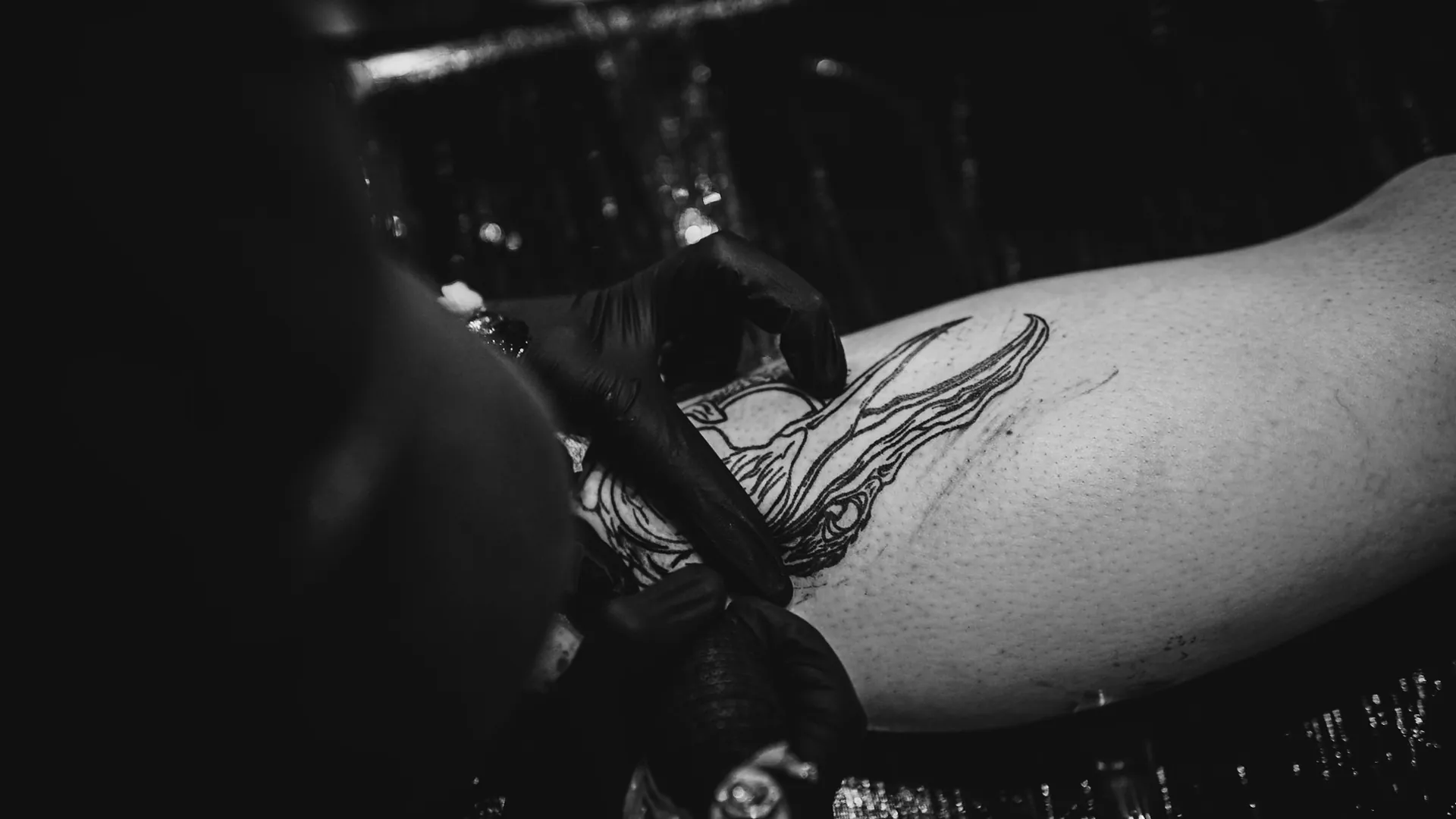 Close do traço de tatuagem sendo puxado sobre o estêncil na perna, em luz quente e baixa