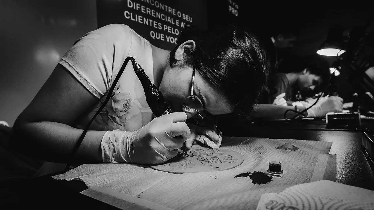 Aluna de óculos e luvas tatuando pele sintética no P&B Vazio, com sombras mais fundas